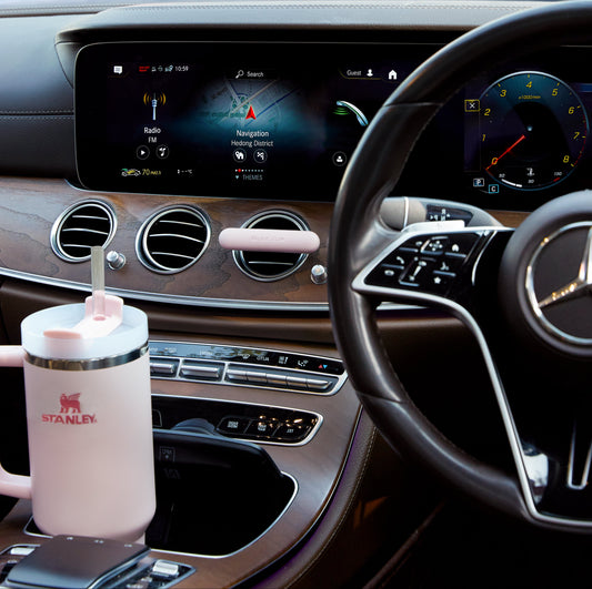 Mercedes-Benz Luxury car interior dashboard with navigation screen, steering wheel, and pink Stanley mug in cup holder and pink leather Maison Aire car diffuser 