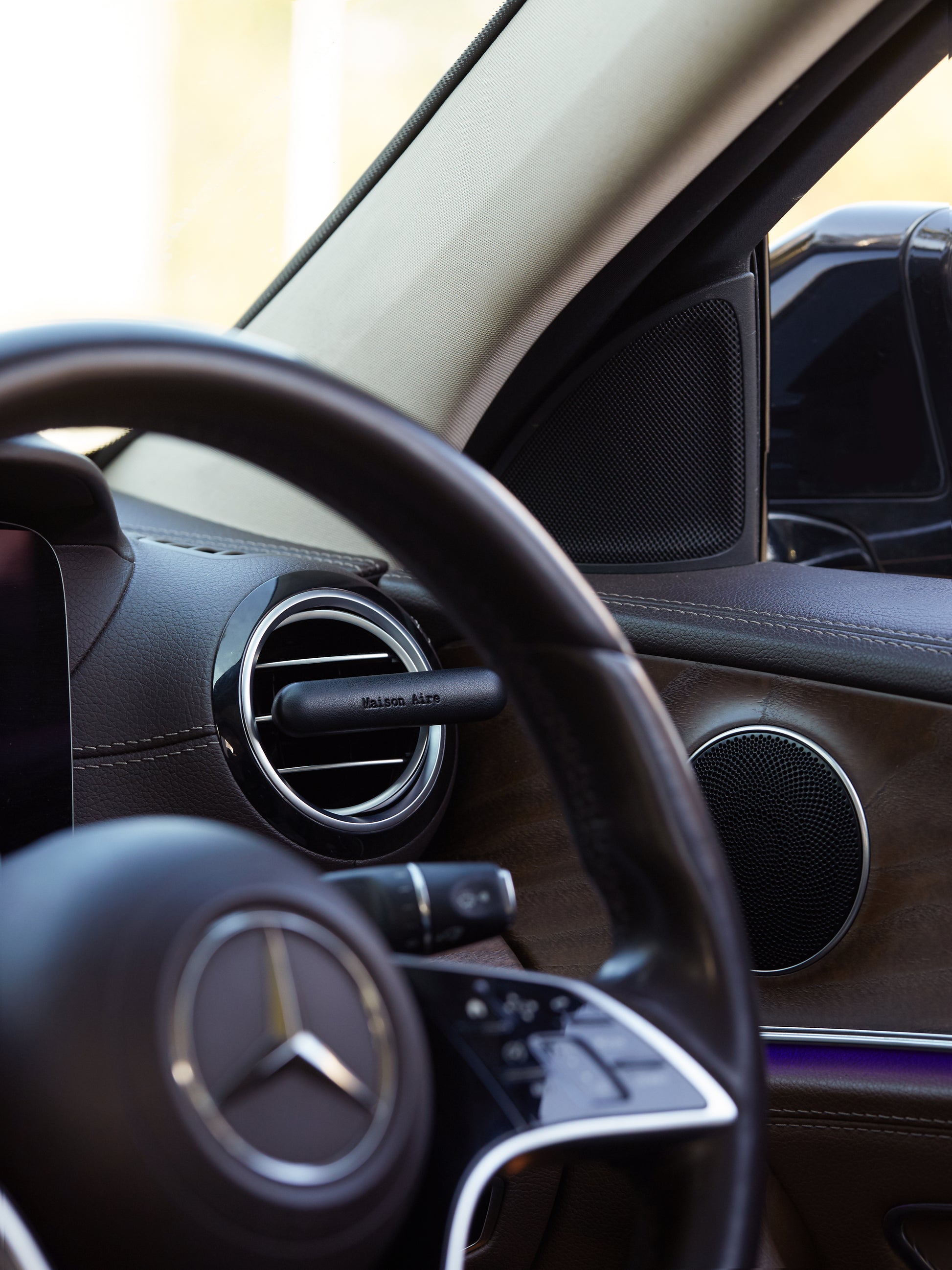 Close-up of Mercedes-Benz steering wheel and car interior with a black leather Maison Aire air diffuser freshener on vent