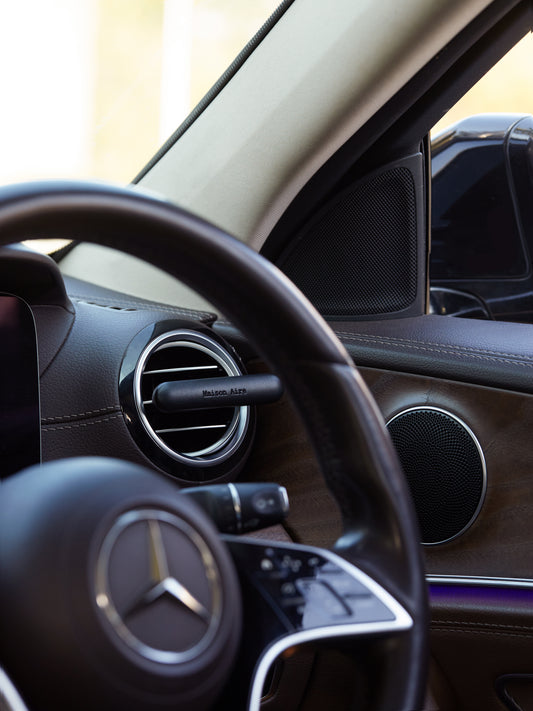 Close-up of Mercedes-Benz steering wheel and car interior with a black leather Maison Aire air diffuser freshener on vent