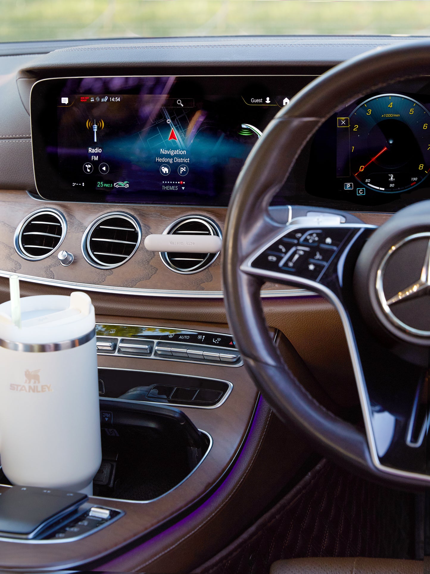 Mercedes-Benz Luxury car interior dashboard with navigation screen, steering wheel, and grey Stanley mug in cup holder and a grey leather Maison Aire car diffuser 