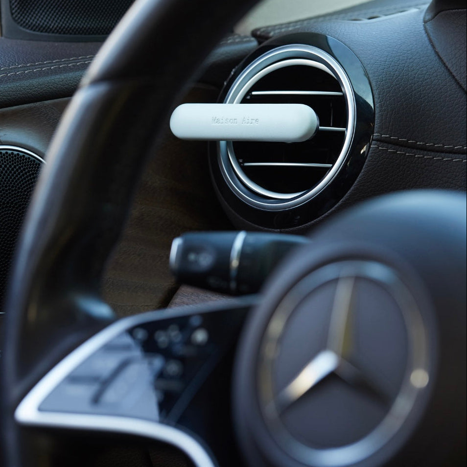 Maison Aire baby blue leather car air freshener attached to a circular air vent in a Mercedes-Benz interior