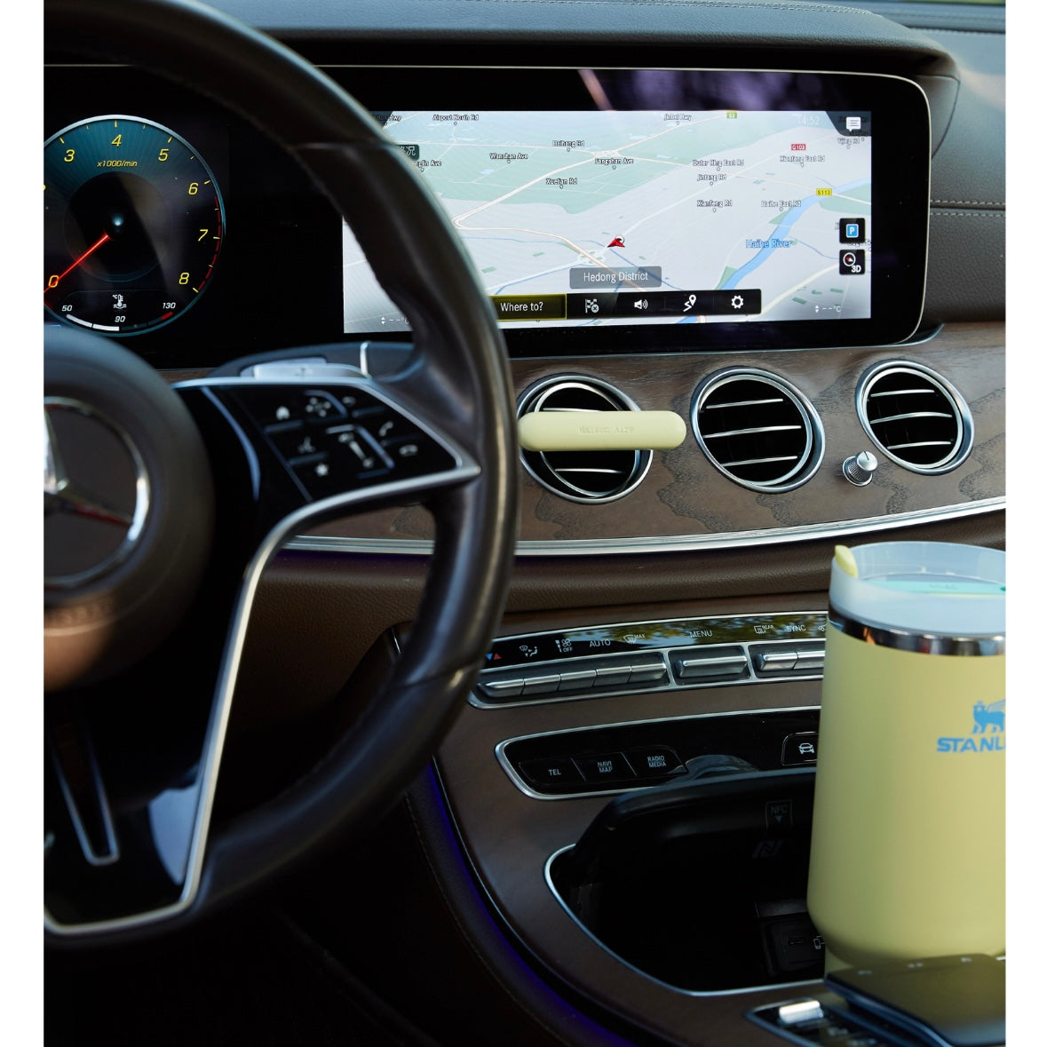 Mercedes-Benz Luxury car interior dashboard with navigation screen, steering wheel, and yellow Stanley mug in cup holder and butter yellow leather Maison Aire car diffuser 